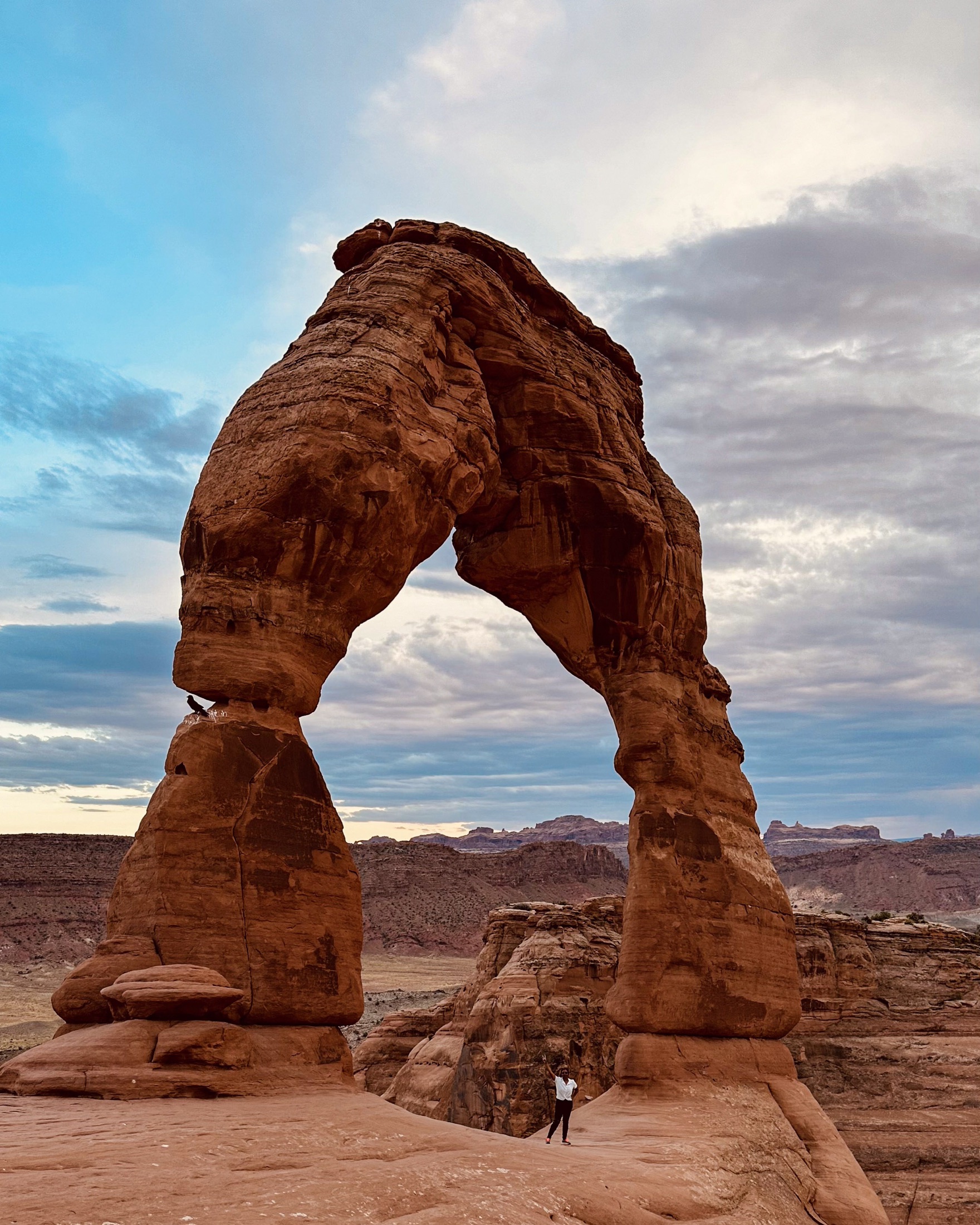 Delicate Arch beneath a dramatic evening sky with a traveler standing at its base
