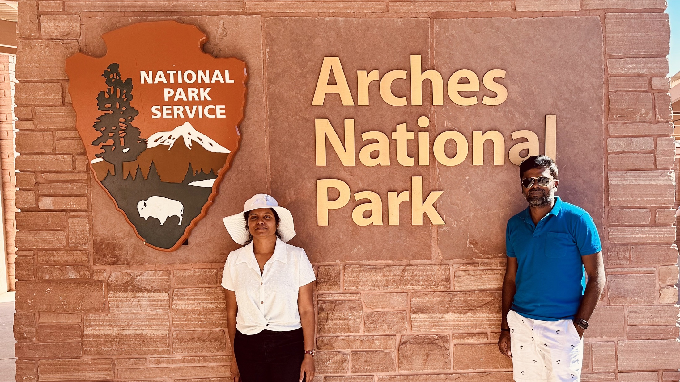 Two travelers standing beside the Arches National Park entrance sign