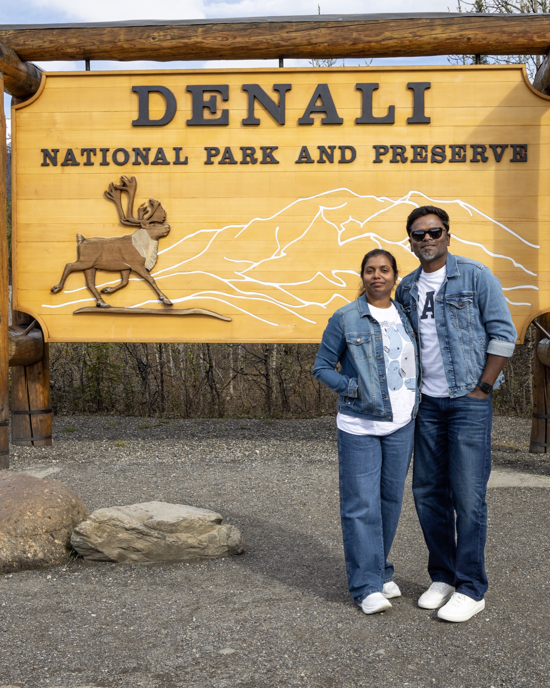 Two travelers standing beside the Denali National Park and Preserve entrance sign