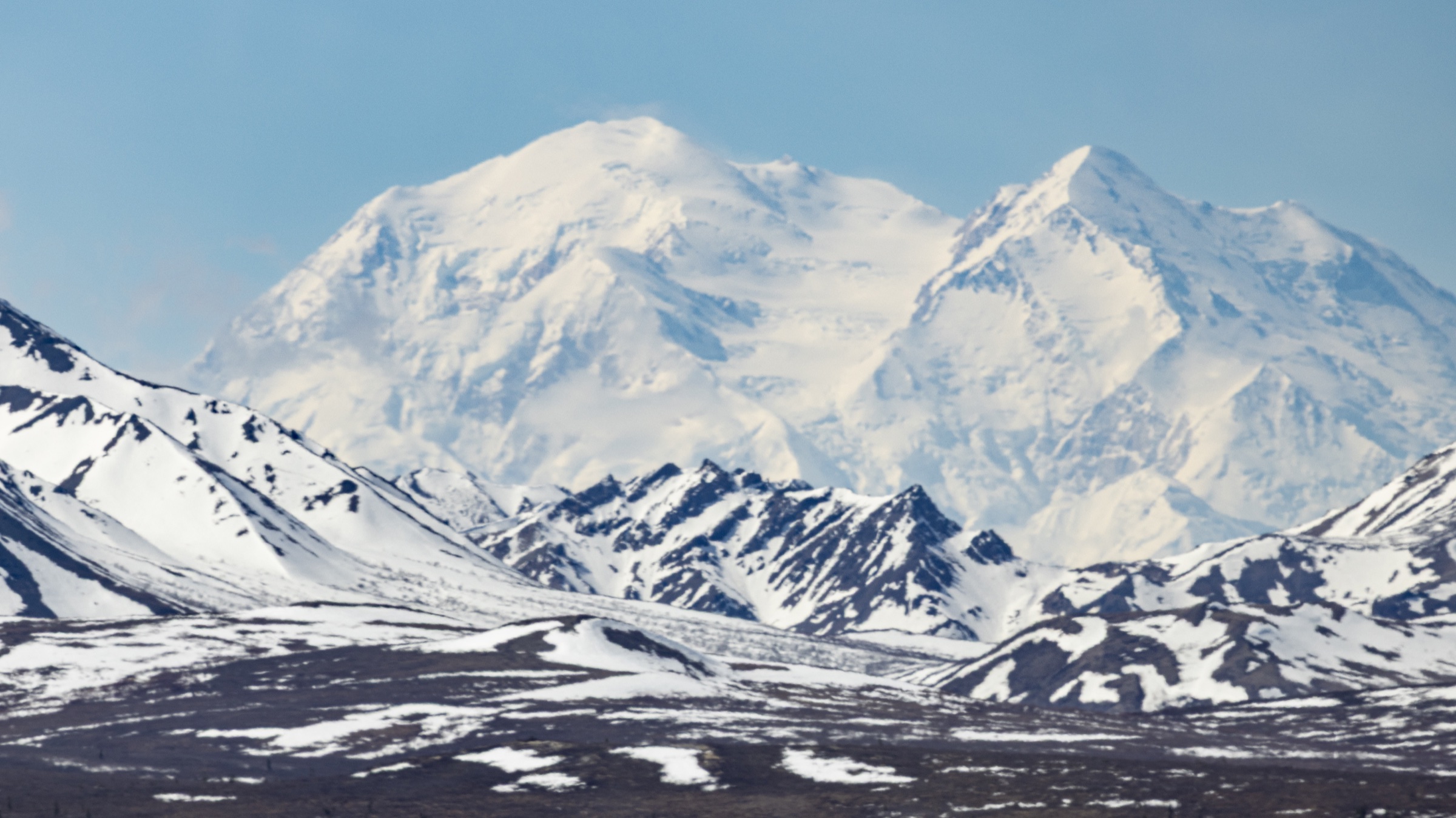 Denali rising above dark, snow-covered ridges beneath a clear blue sky