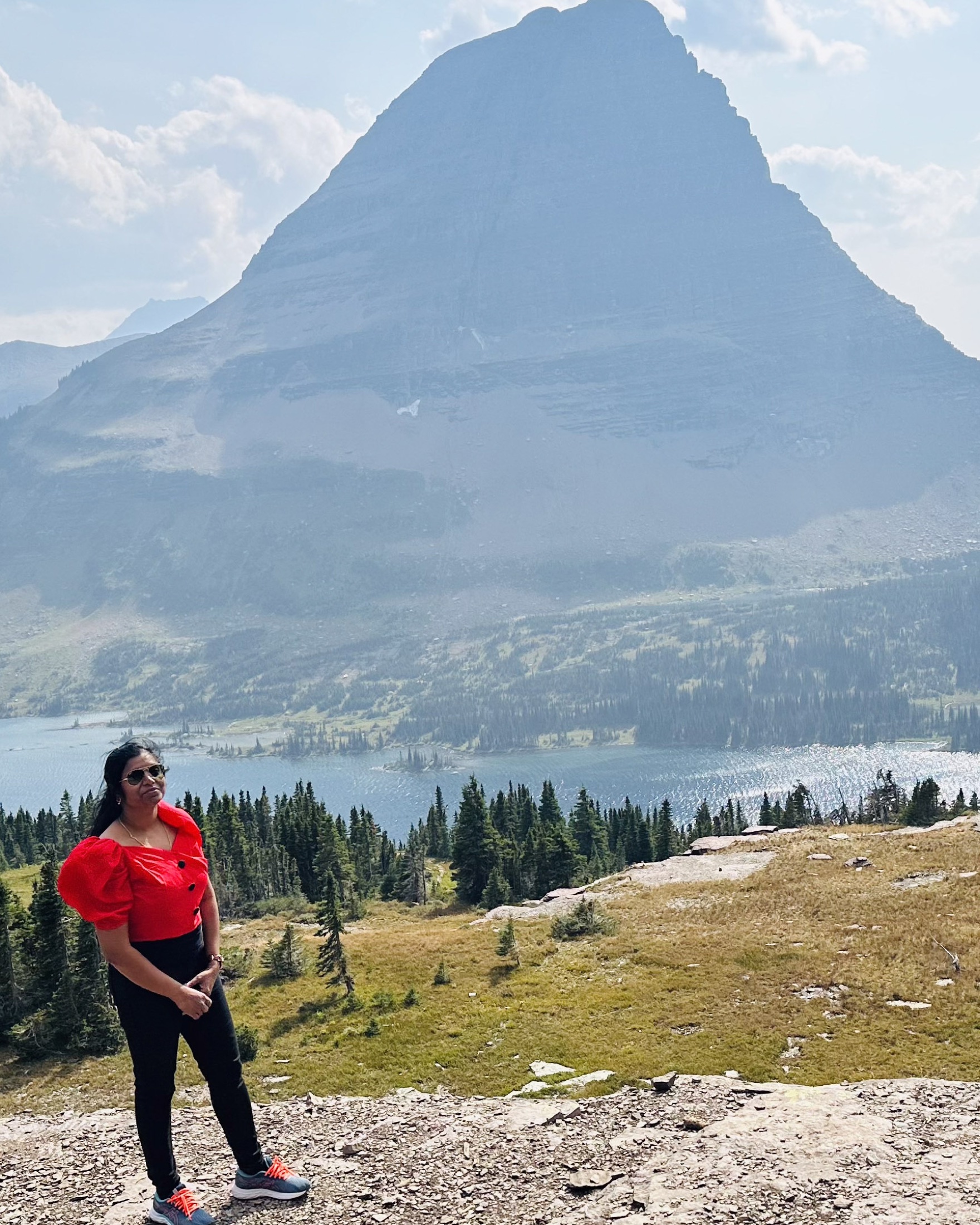 A traveler standing above an alpine lake with a tall mountain rising behind her in Glacier National Park