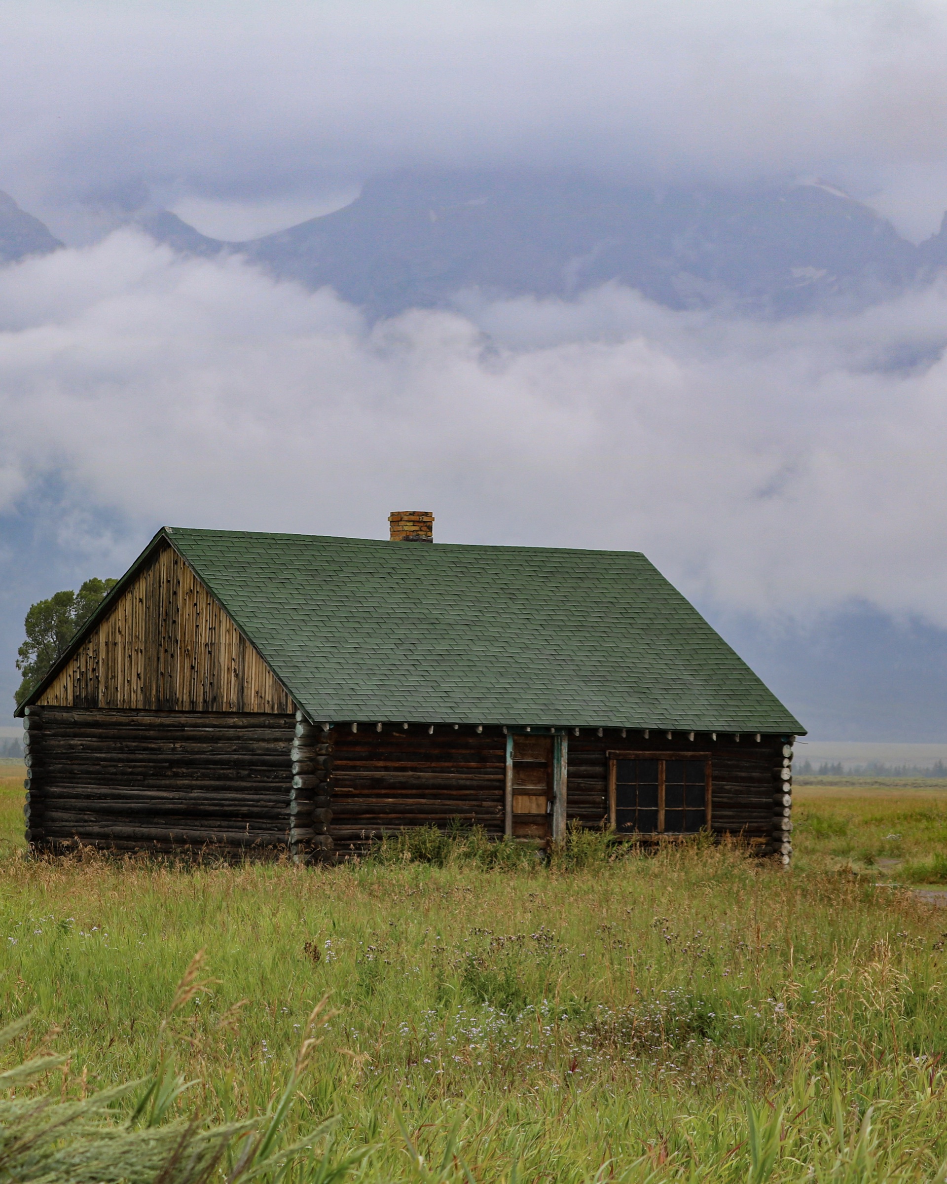 A historic cabin beneath cloud-wrapped mountains in Grand Teton National Park